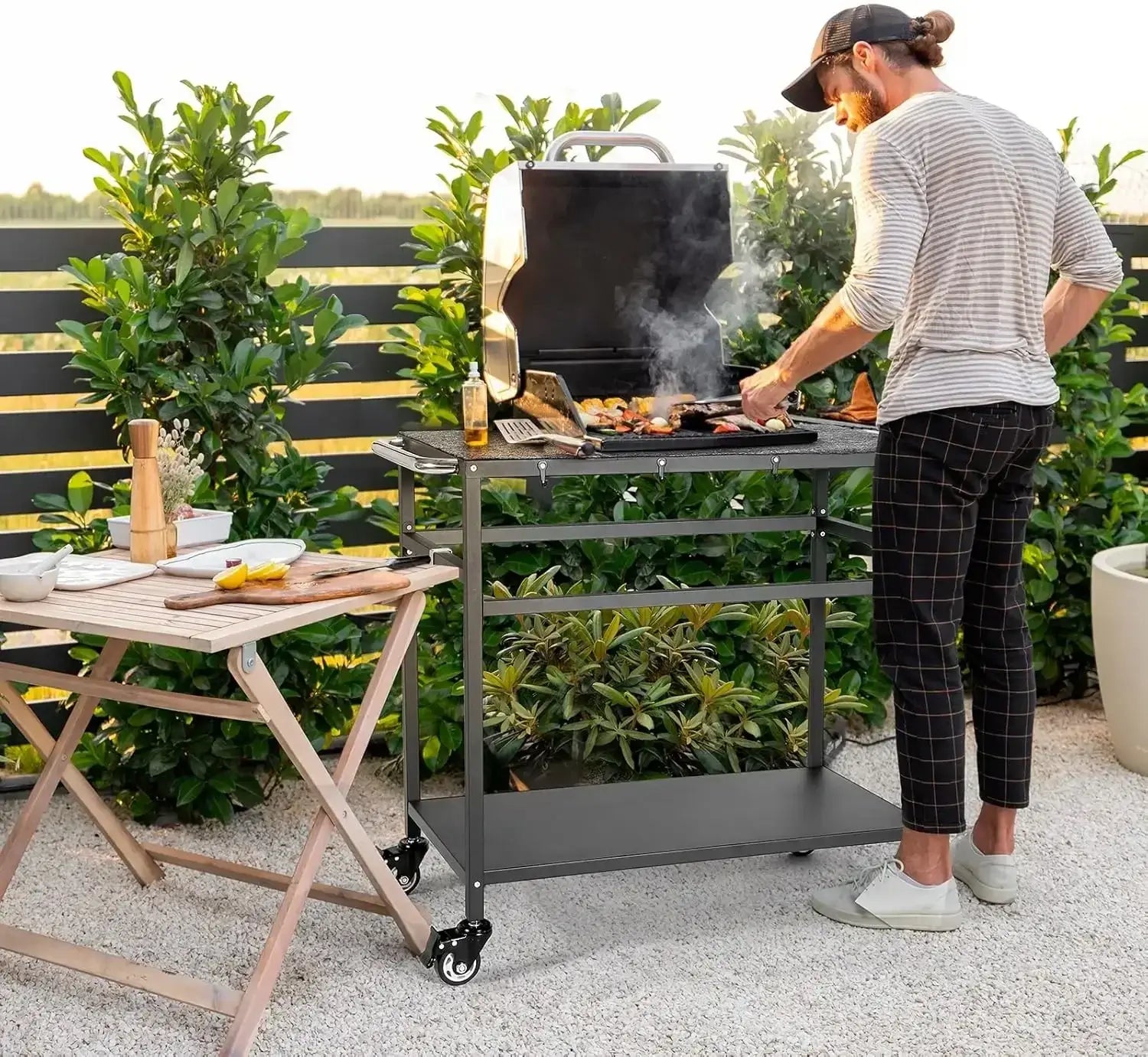 Outdoor grill table with storage on wheels in use on a patio, featuring grill mats and spacious shelves for convenient outdoor cooking.