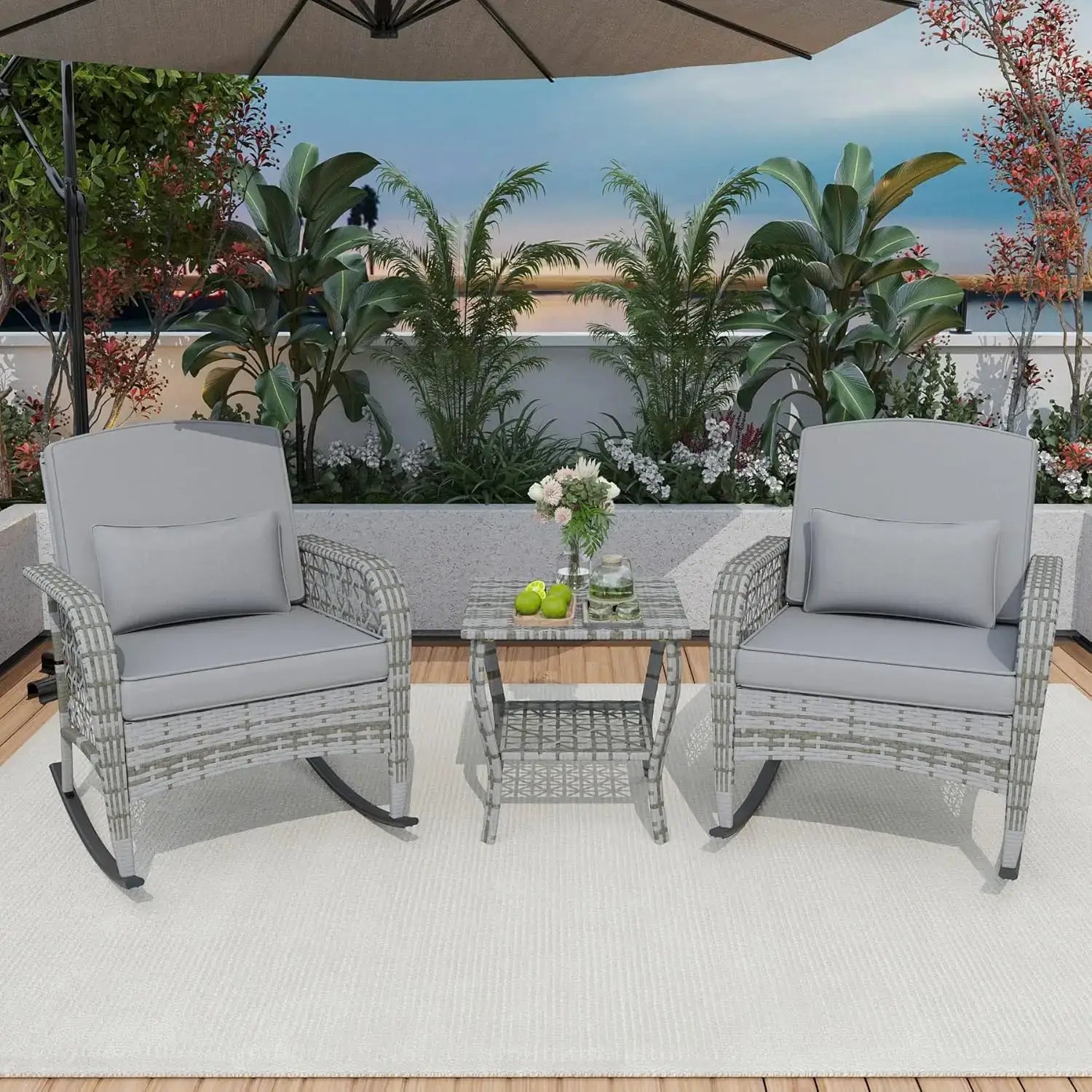 Gray cushioned 3-piece patio rocking chair set with rattan design, placed on a wooden deck with greenery in the background.