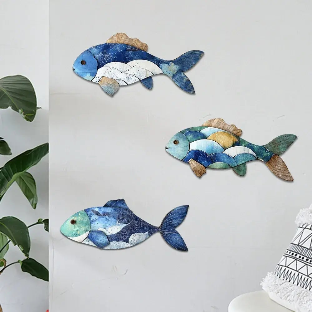 Three handcrafted wooden fish wall decorations in blue and brown tones on a white wall. Ideal for coastal home and garden accents.