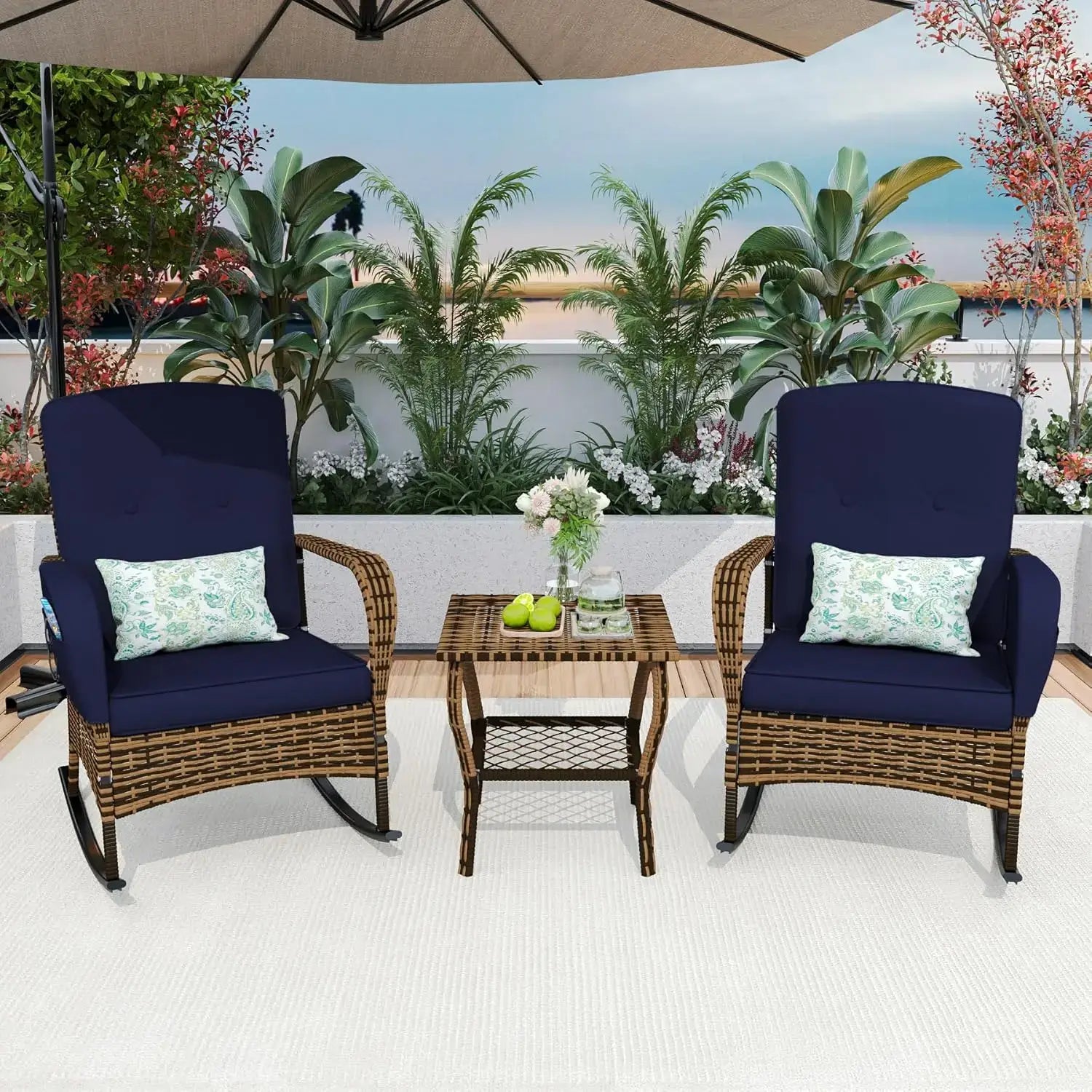Navy blue cushion 3-piece patio rocking chair set with rattan frame and floral pillows, styled on a rooftop deck with lush plants.
