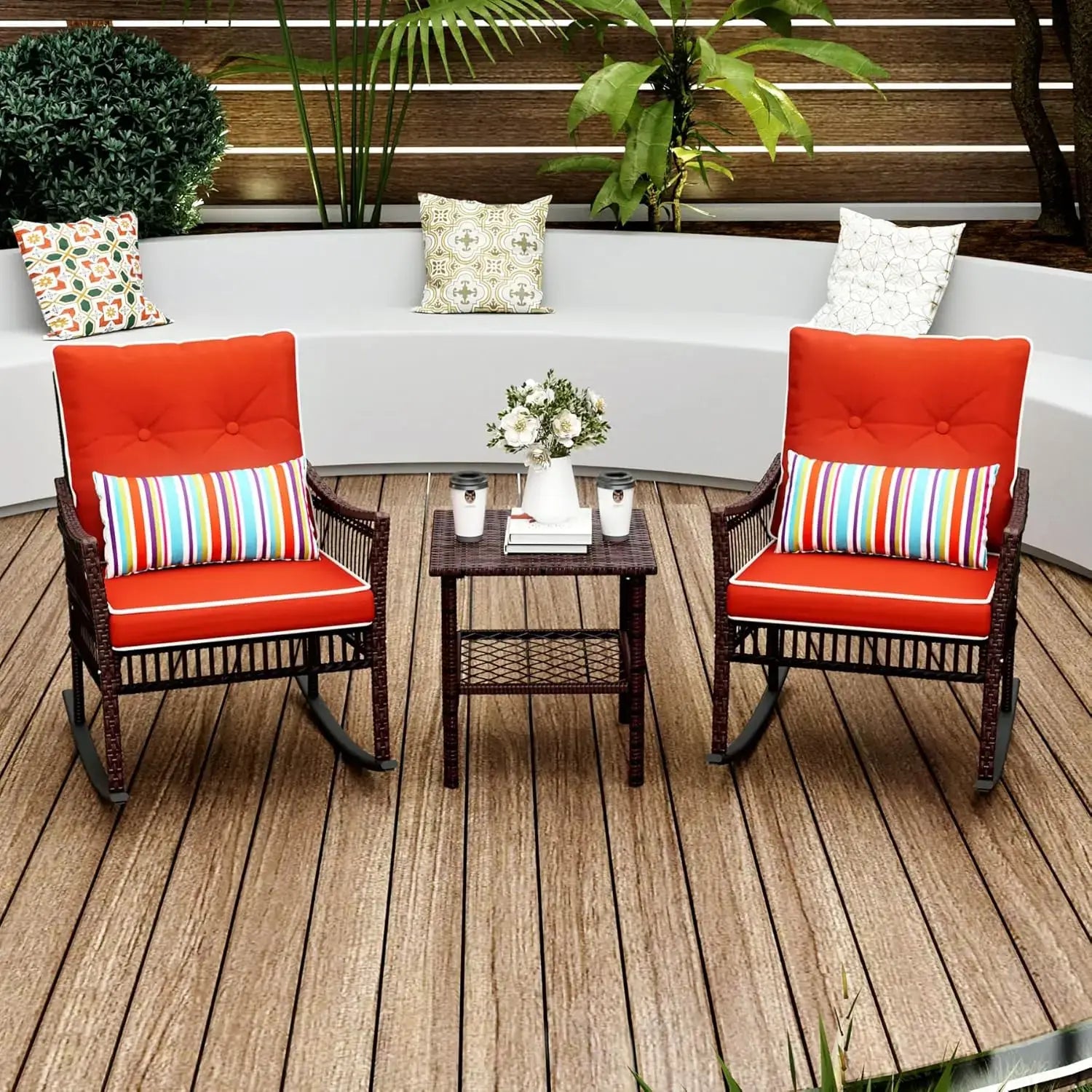 Red cushioned 3-piece patio rocking chair set with striped pillows and rattan table, arranged on a wood deck with curved seating.