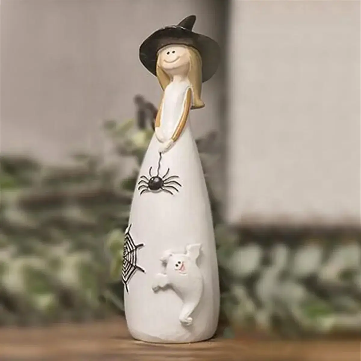 Halloween Witch Figurine - Enchanting Decor | Resin Craft featuring a smiling witch in a black hat with spider, web, and ghost details on white dress. Ideal for spooky seasonal home accents.